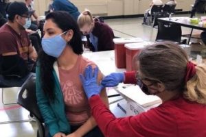 A healthcare worker delivers a shot in the arm of a masked woman.