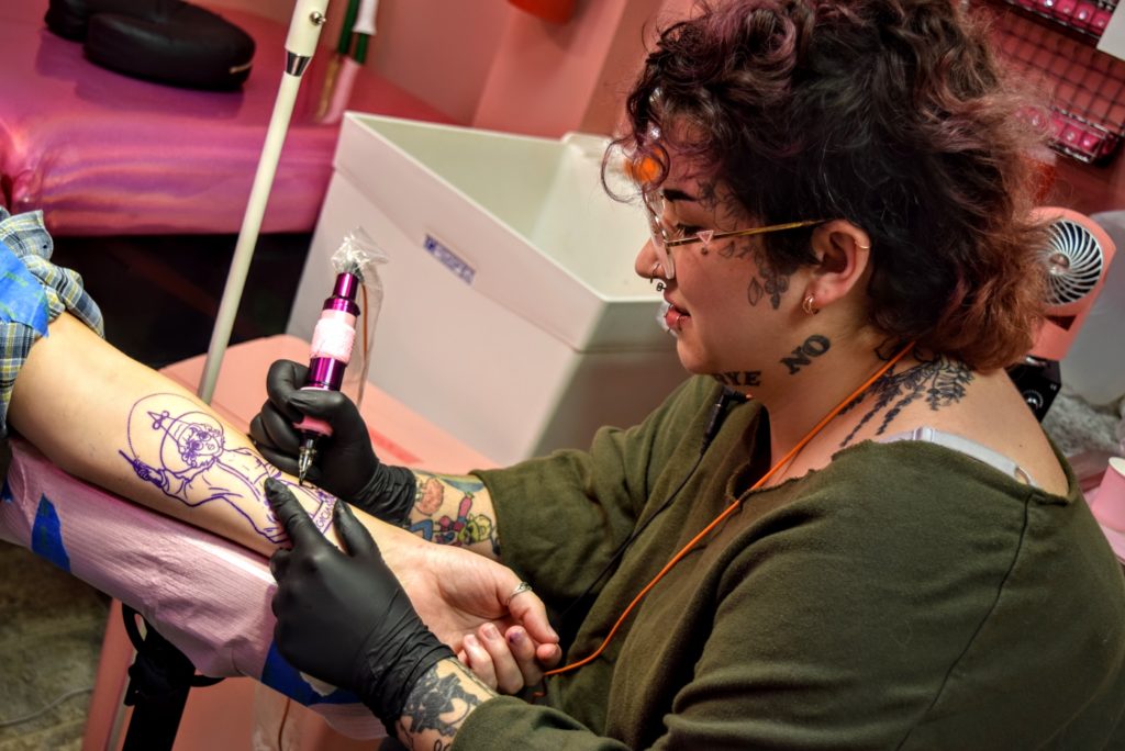 Picture shows Tempest creating a tattoo on a persons forearm